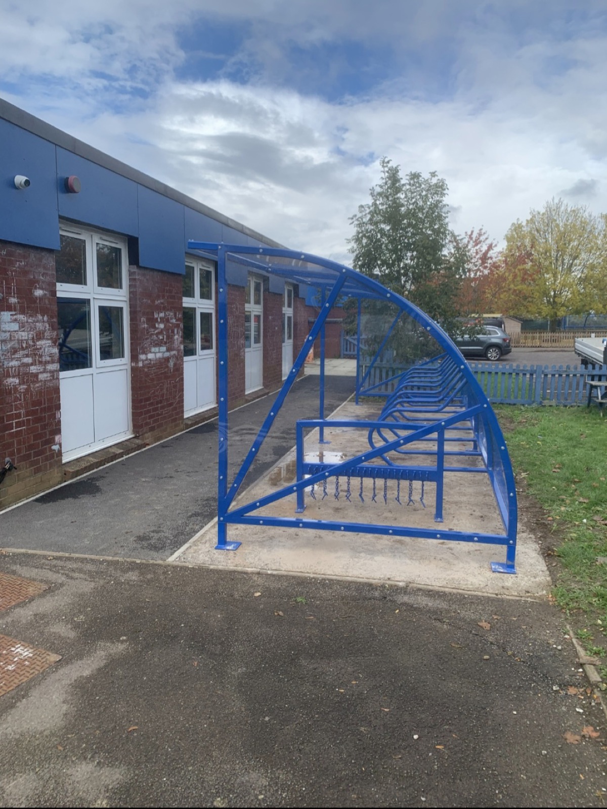 Blue cycle shelter with a scooter rack by a brick building