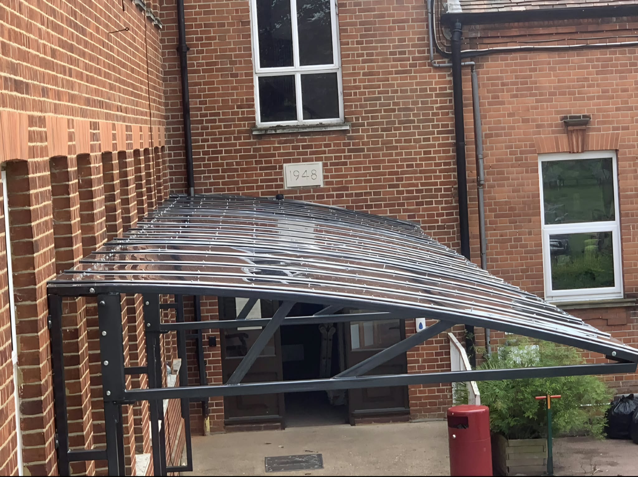 Black curved dining canopy with a clear polycarbonate roof against a red-brick building in Hull