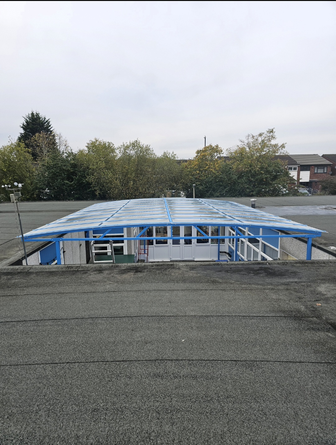 Blue steel canopy with a clear polycarbonate roof covering a school's internal courtyard, seen from the surrounding roof in Lancaster