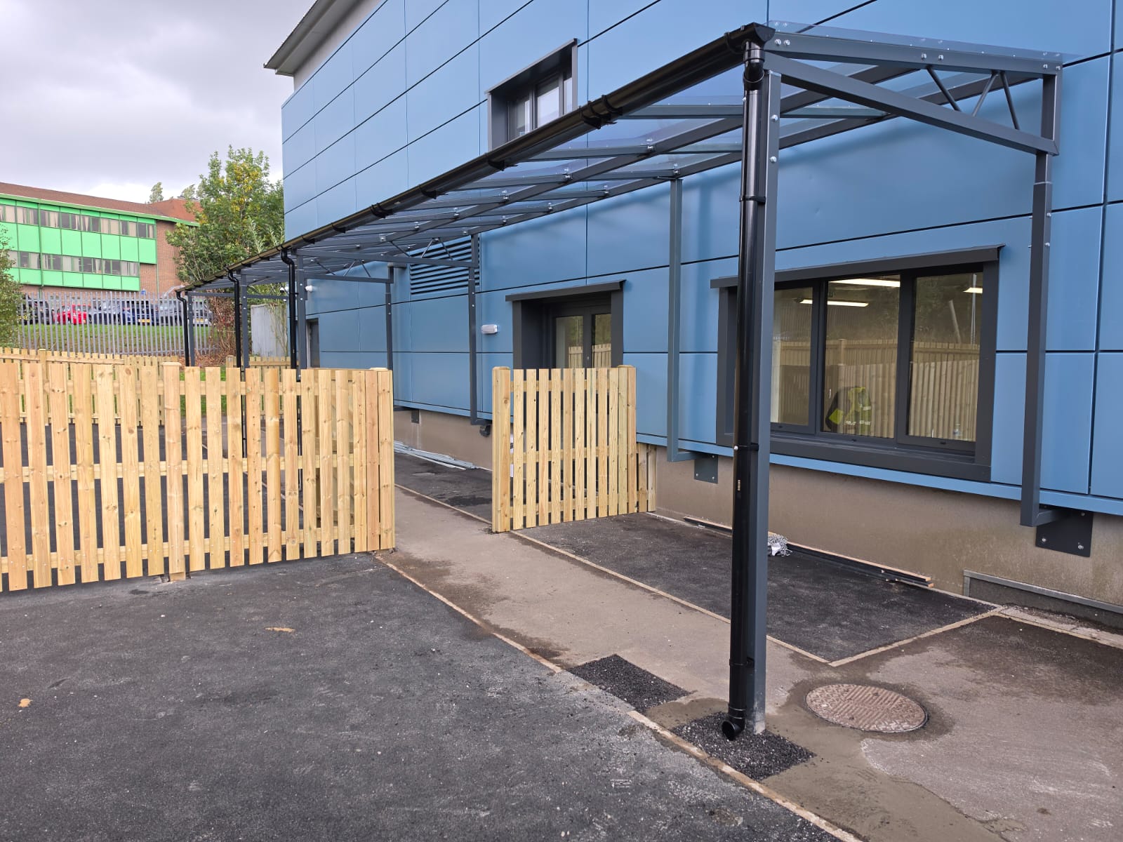 Mono-pitch canopy with glazed roof running along a blue-clad wall at The Deans School, Manchester