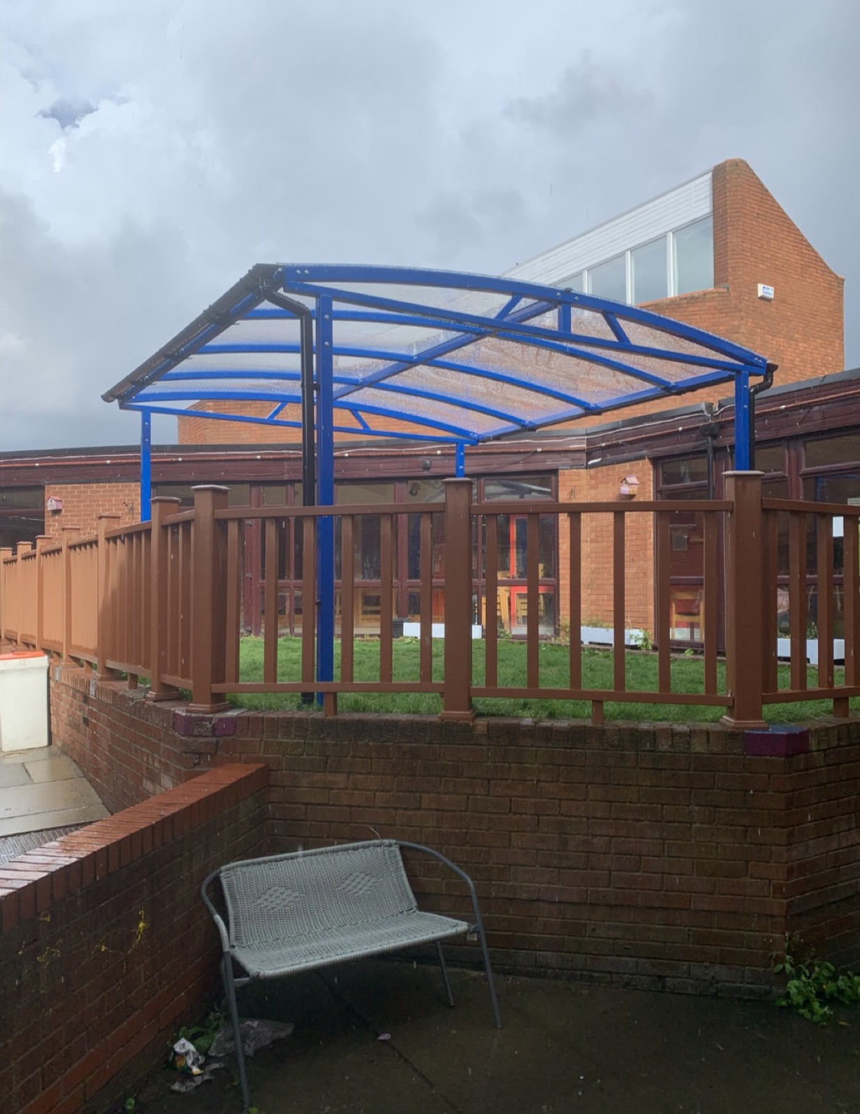 Blue curved-roof shelter behind railings outside a brick building in Leeds