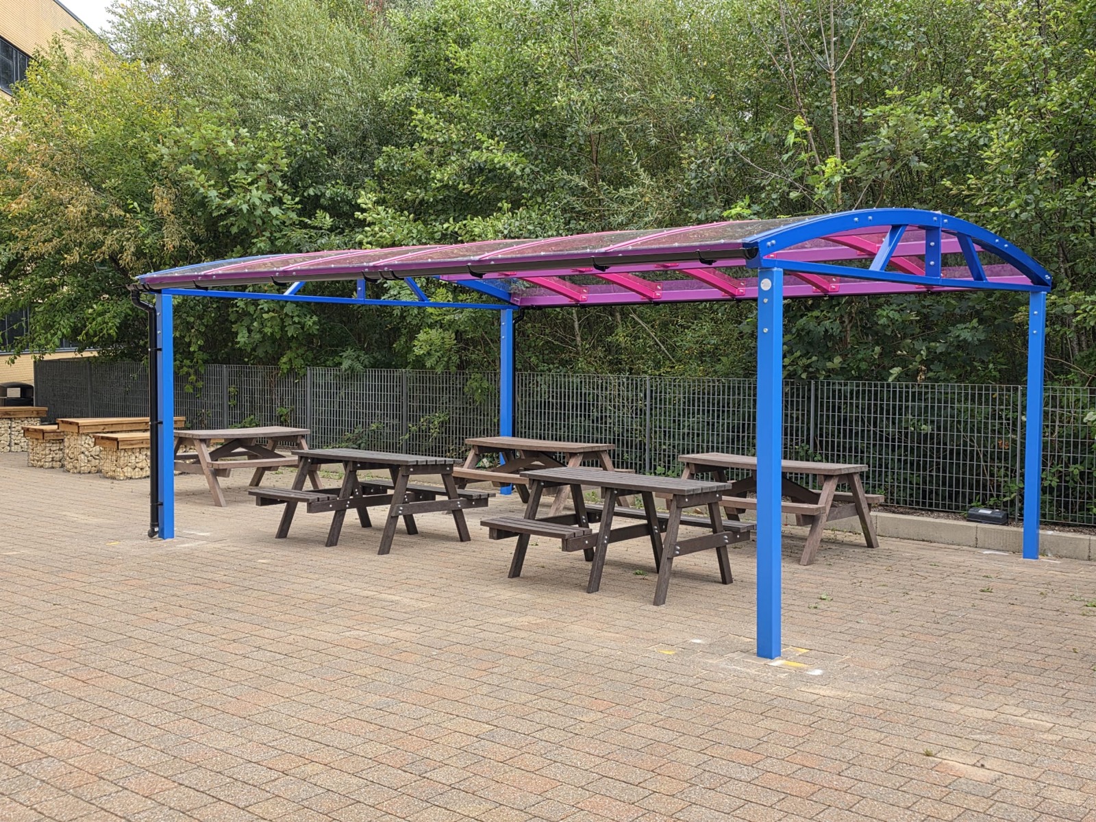 Blue and pink barrel-curved dining canopy over wooden picnic benches at West Lancashire College
